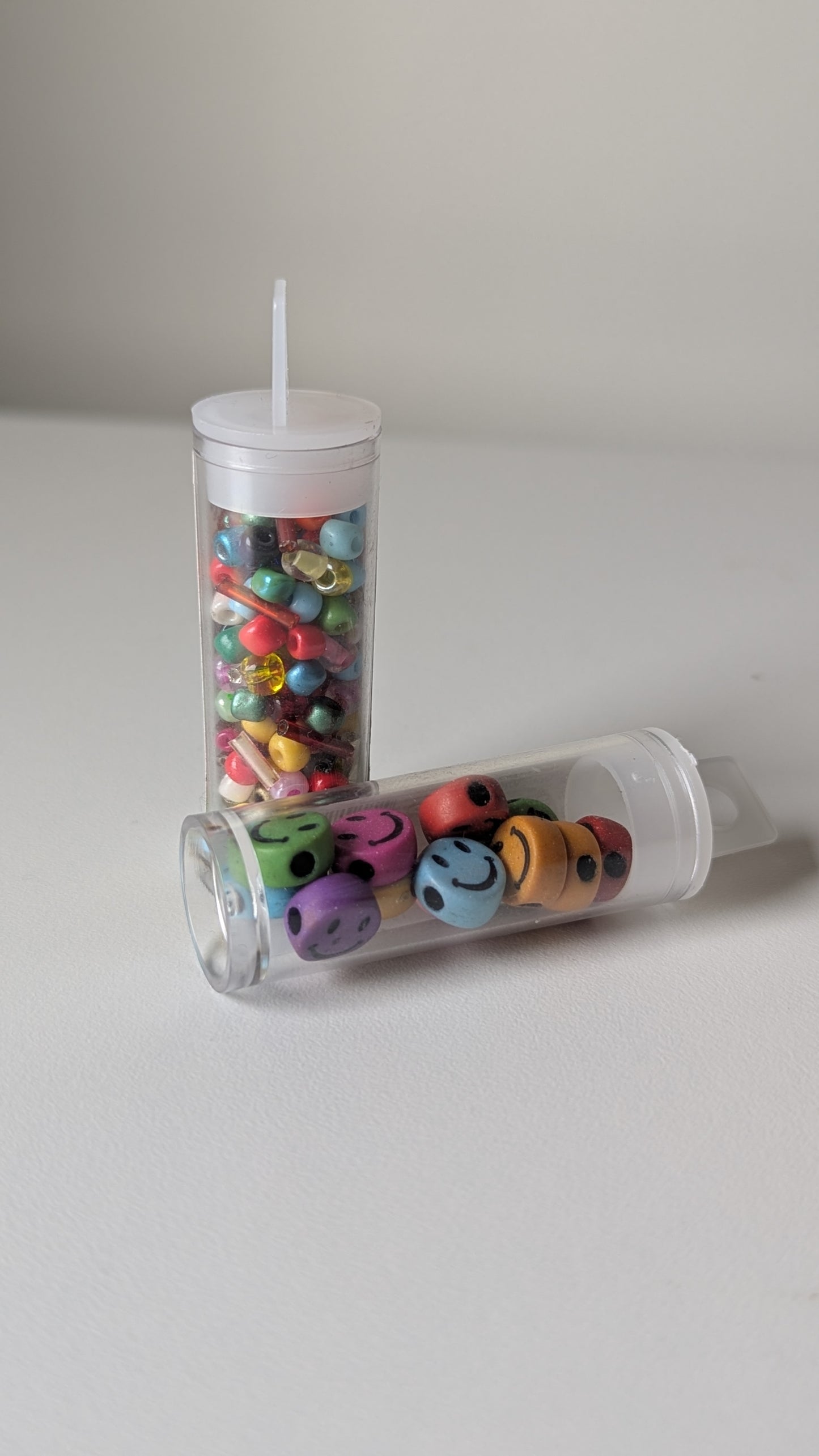 Two clear plastic tubes filled with colorful smiley face beads on a light gray background.