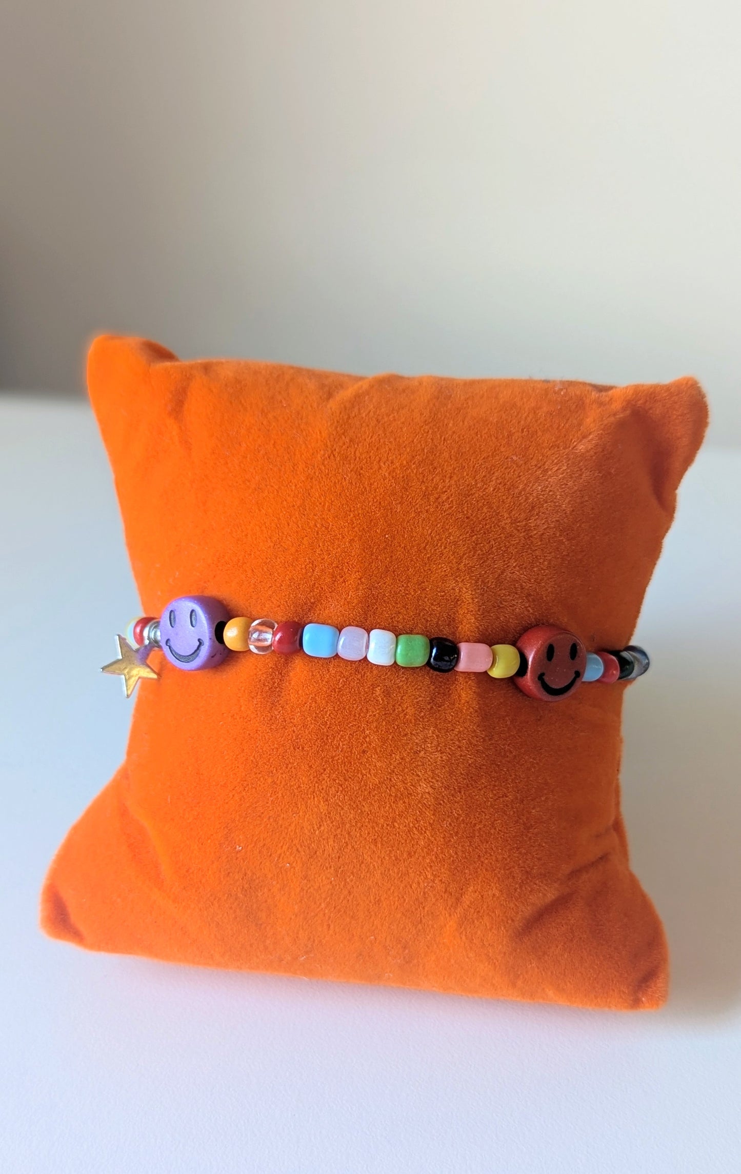 colourful glass beads bracelet with smiley face beads on an orange cushion