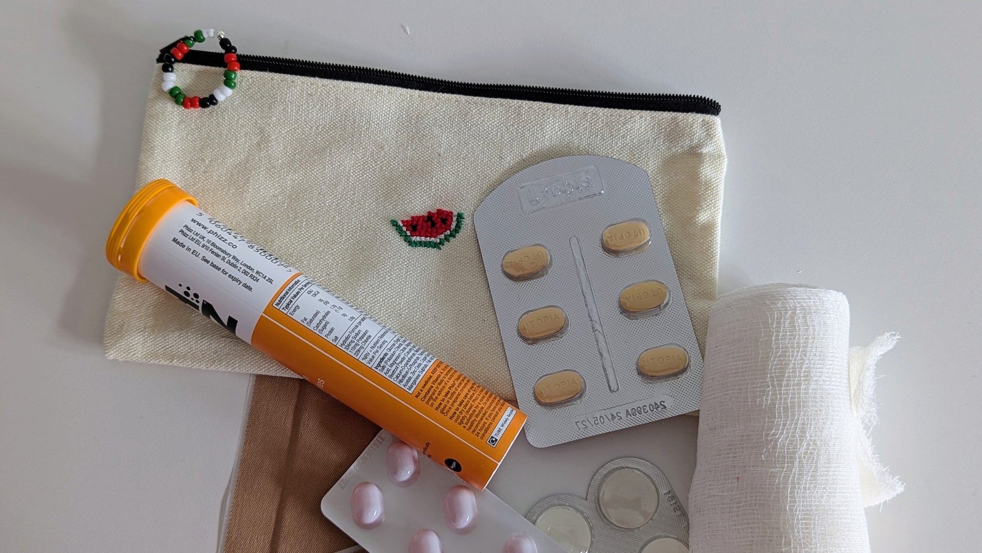 Cotton pouch hand embroidered watermelon, with medical supplies including a tube and pill packaging on a white background